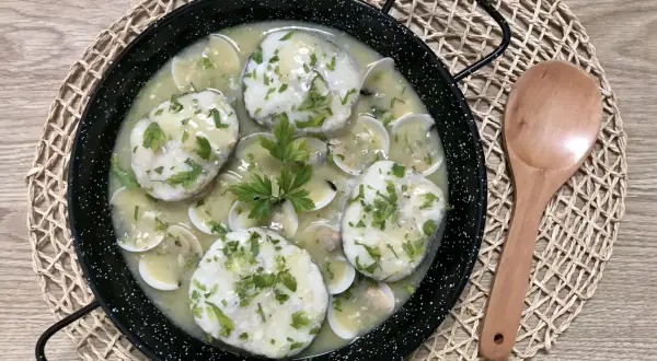 Merluza a la vasca, un plato tradicional con trozos de pescado blanco en una salsa cremosa con almejas y perejil picado.