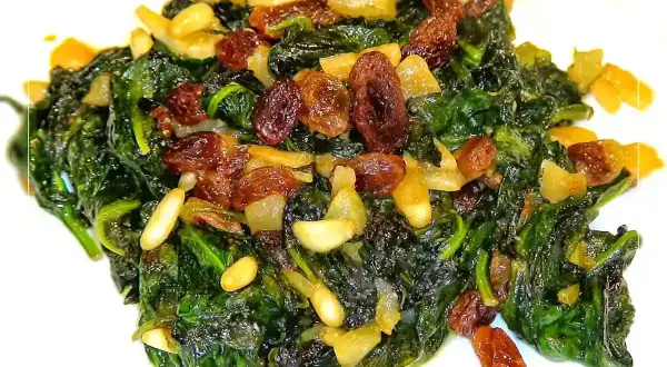 Espinacas a la catalana, un plato vibrante con espinacas salteadas, pasas dulces y piñones tostados.