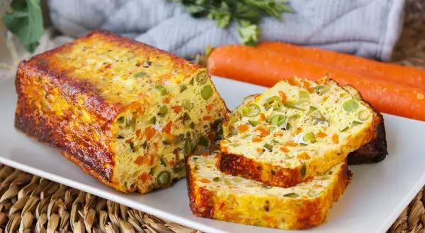 Pastel de verduras casero, con trozos visibles de zanahoria y guisantes, servido en una bandeja blanca.