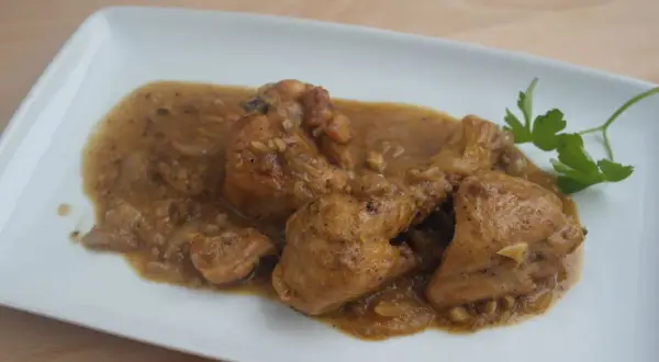 Sabroso pollo con almendras en una salsa dorada, servido en un plato blanco con una ramita de perejil.