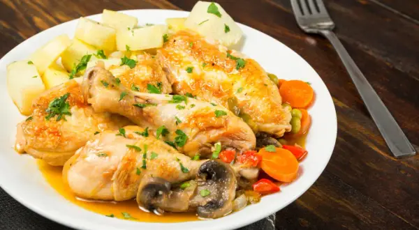 Sabroso pollo a la pepitoria con patatas, zanahorias, guisantes y champiñones, todo espolvoreado con perejil fresco.