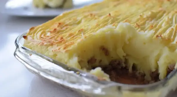 Un delicioso pastel de papa recién horneado, con una capa dorada y texturizada de puré de papa sobre un relleno jugoso.