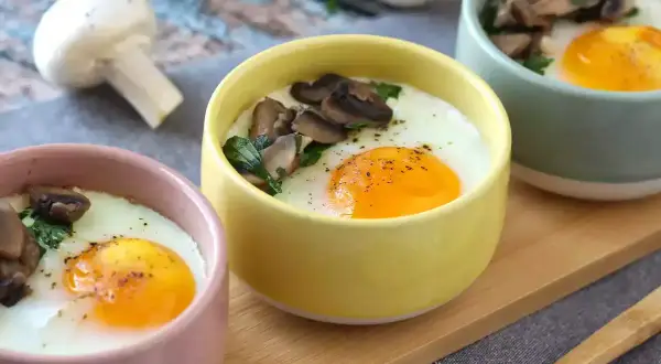 Deliciosos huevos al horno con champiñones y perejil, servidos en coloridas tazas. Un desayuno perfecto.