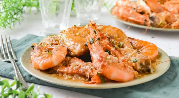 Plato de pollo con gambas en salsa cremosa, decorado con perejil picado. Un manjar listo para disfrutar.