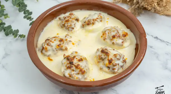 Huevos rellenos gratinados con bechamel y queso, servidos en una cazuela de barro.