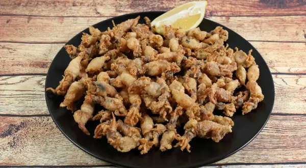Un plato negro rebosante de puntillas de calamar crujientes, con un gajo de limón esperando para dar el toque final.