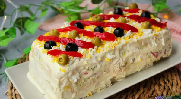 Pastel de atún decorado con pimientos rojos, aceitunas negras y verdes, y huevo rallado. ¡Una delicia para compartir!