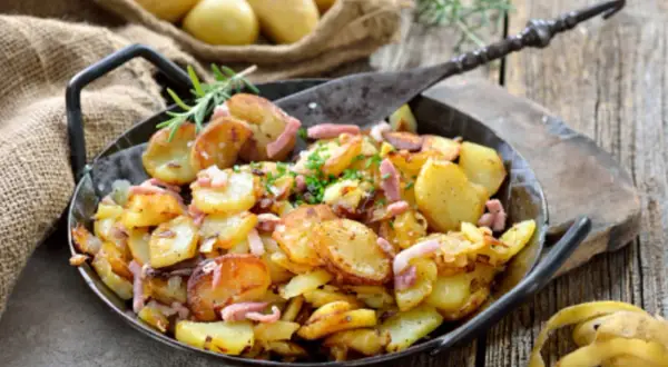 Patatas con bacon y queso, doradas y crujientes, servidas en una sartén de hierro fundido. Un plato perfecto para compartir.