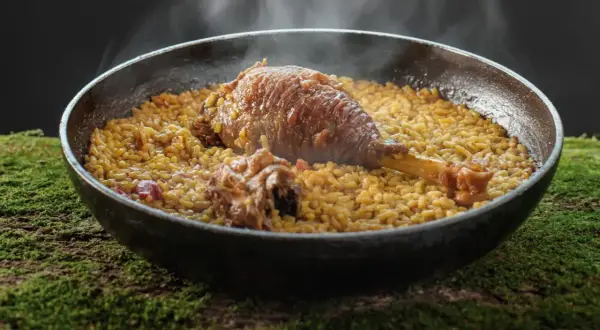 Arroz meloso con pitu de caleya, humeante y servido en paellera sobre un lecho de musgo.