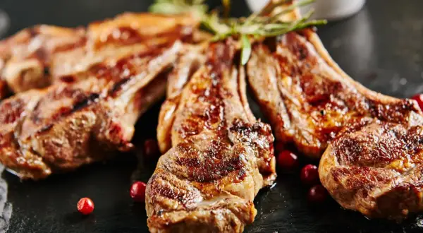Chuletillas al sarmiento, jugosas y doradas, servidas con bayas rojas y romero sobre pizarra.