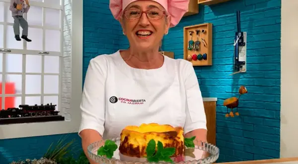 Eva Arguiñano sonríe con su delantal blanco y un gorro rosa, presentando una deliciosa tarta de queso.