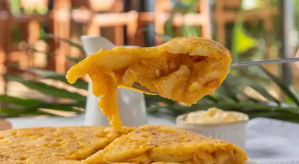 Un tenedor levanta un trozo jugoso de pincho de tortilla, mostrando su interior de patatas y huevo.