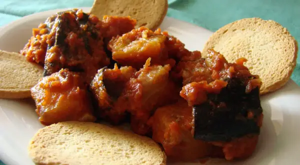 Berenjenas con tomate, un plato casero servido con tostas crujientes.