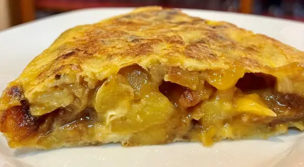 Un trozo jugoso de tortilla de patatas, con patatas tiernas y huevo dorado, servido en un plato blanco.