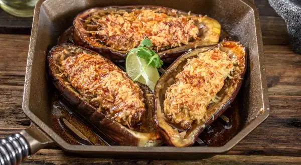 Berenjenas rellenas airfryer doradas y gratinadas, servidas en una sartén de hierro fundido con una rodaja de lima.