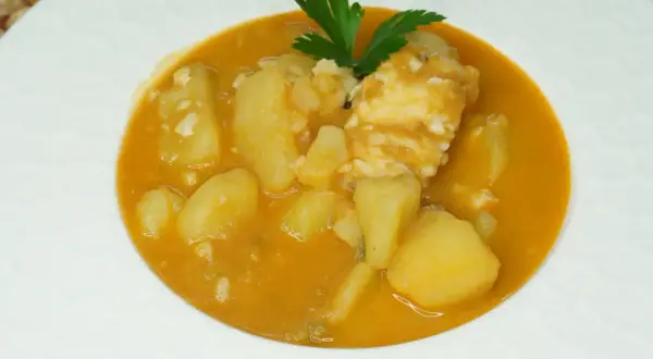 Un plato de patatas con bacalao en una salsa naranja, decorado con perejil.