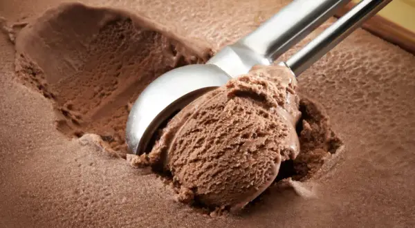 Cuchara saca una porción generosa de helado de chocolate casero, con textura cremosa y color intenso.