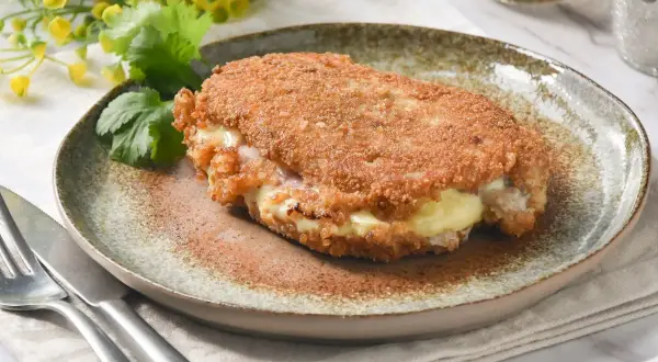 Libritos de lomo empanados, rellenos de queso y jamón, servidos en un plato rústico con cilantro y flores amarillas.