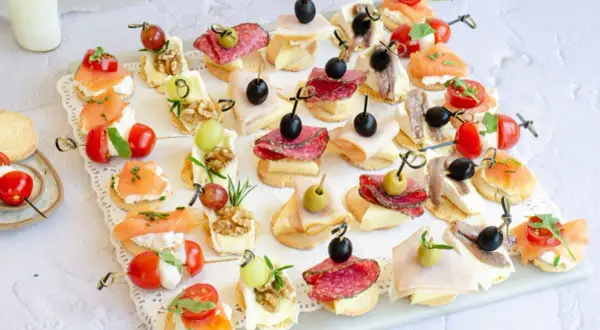 Variedad de canapés fríos fáciles y baratos: salmón, salami, jamón, queso, aceitunas, tomates cherry y más, perfectos para cualquier ocasión.