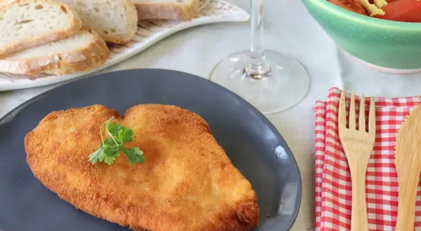 Un delicioso escalope de pollo dorado, servido con pan, ensalada y vino blanco.