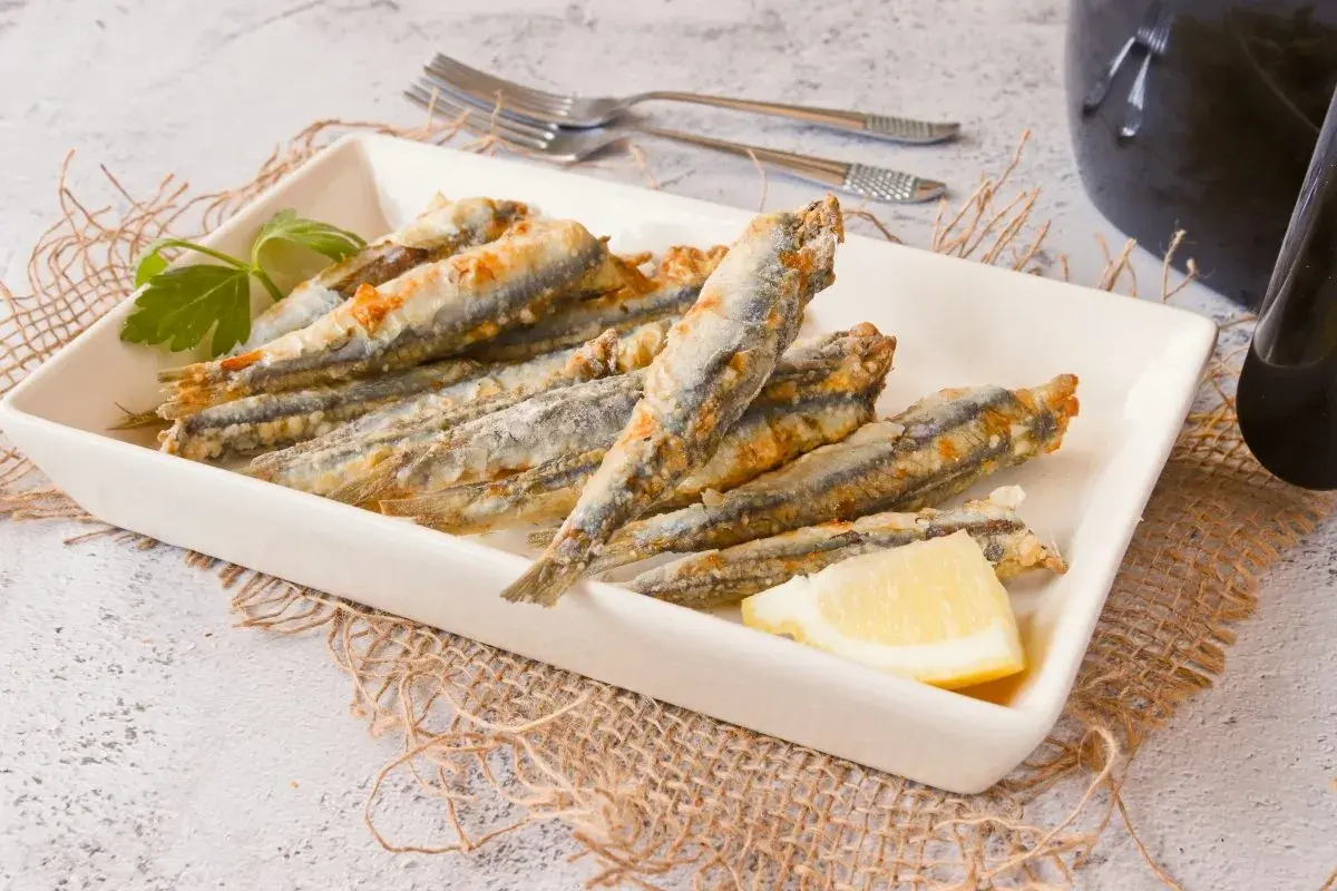 Boquerones en freidora de aire, dorados y crujientes, servidos en plato blanco con limón y perejil.