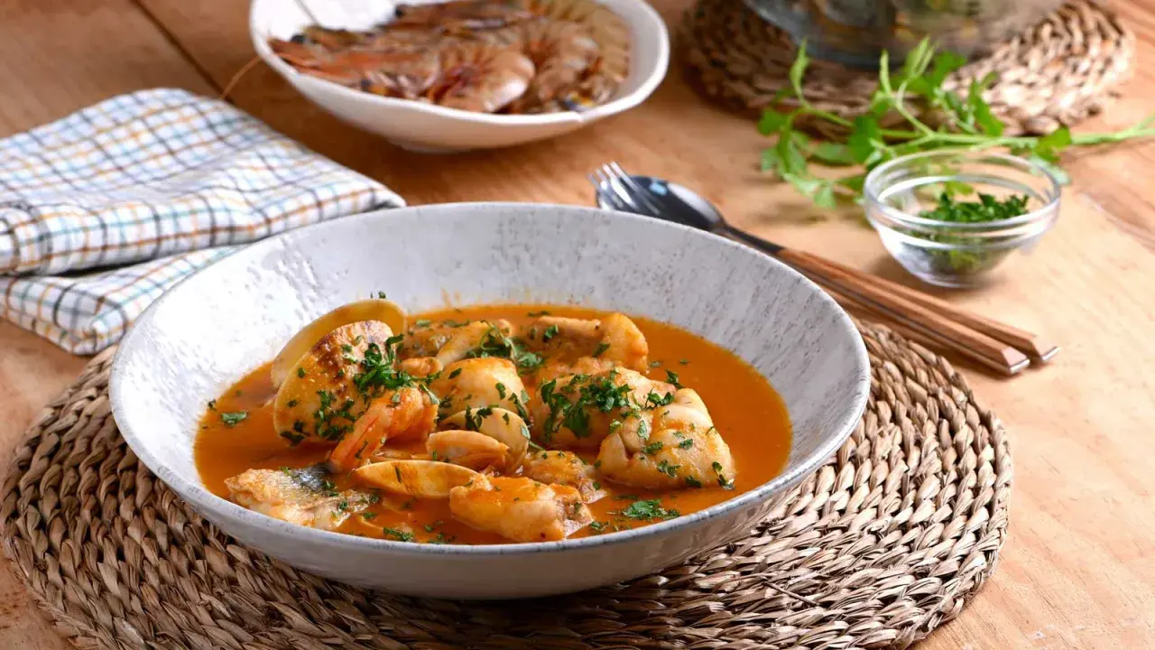 Deliciosa cazuela de pescado con gambas y trozos de pescado blanco en una salsa rojiza, adornada con perejil fresco.