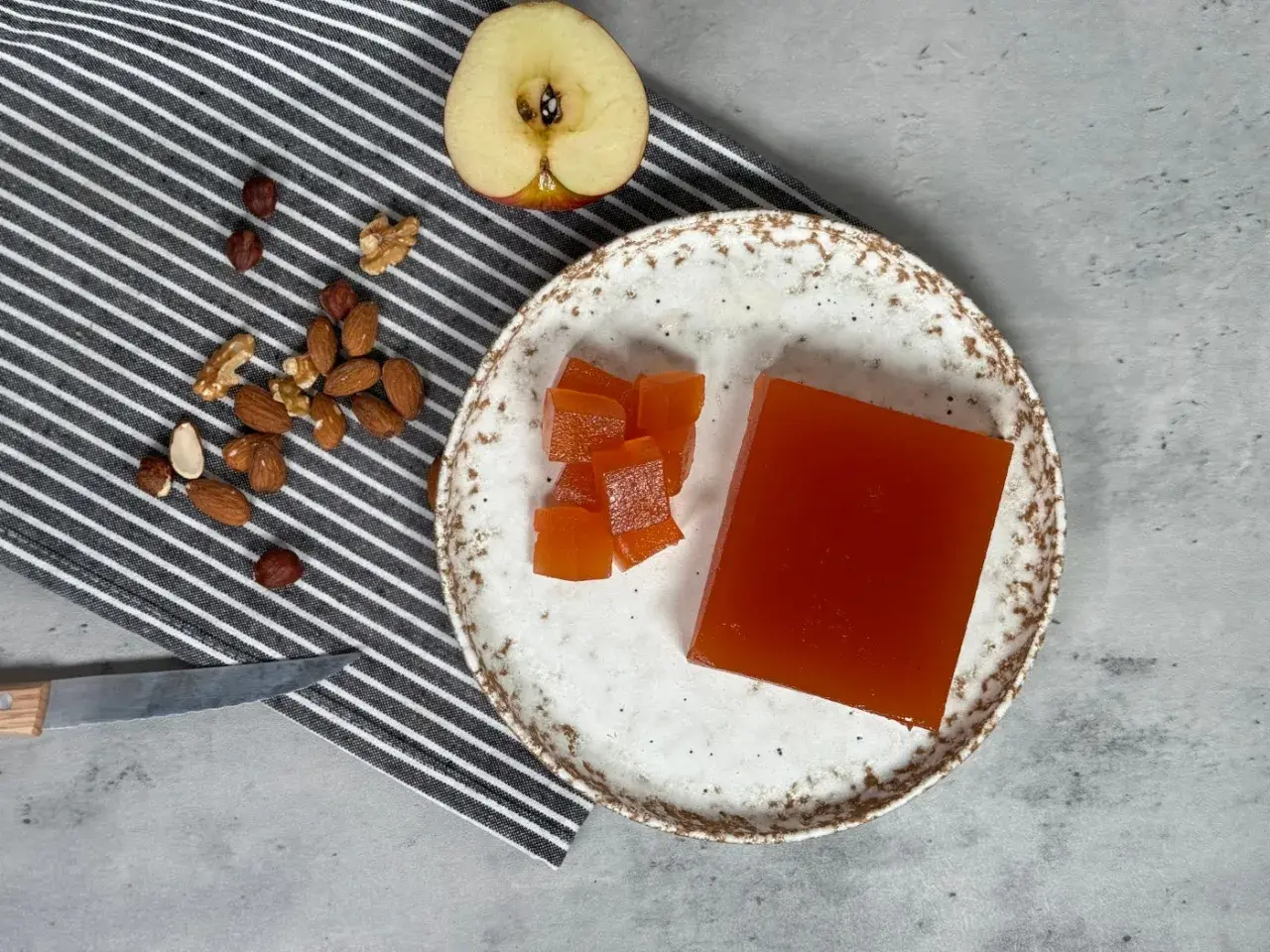 Un trozo de dulce de manzana y cubos cortados en un plato, junto a frutos secos y una manzana a medio cortar.