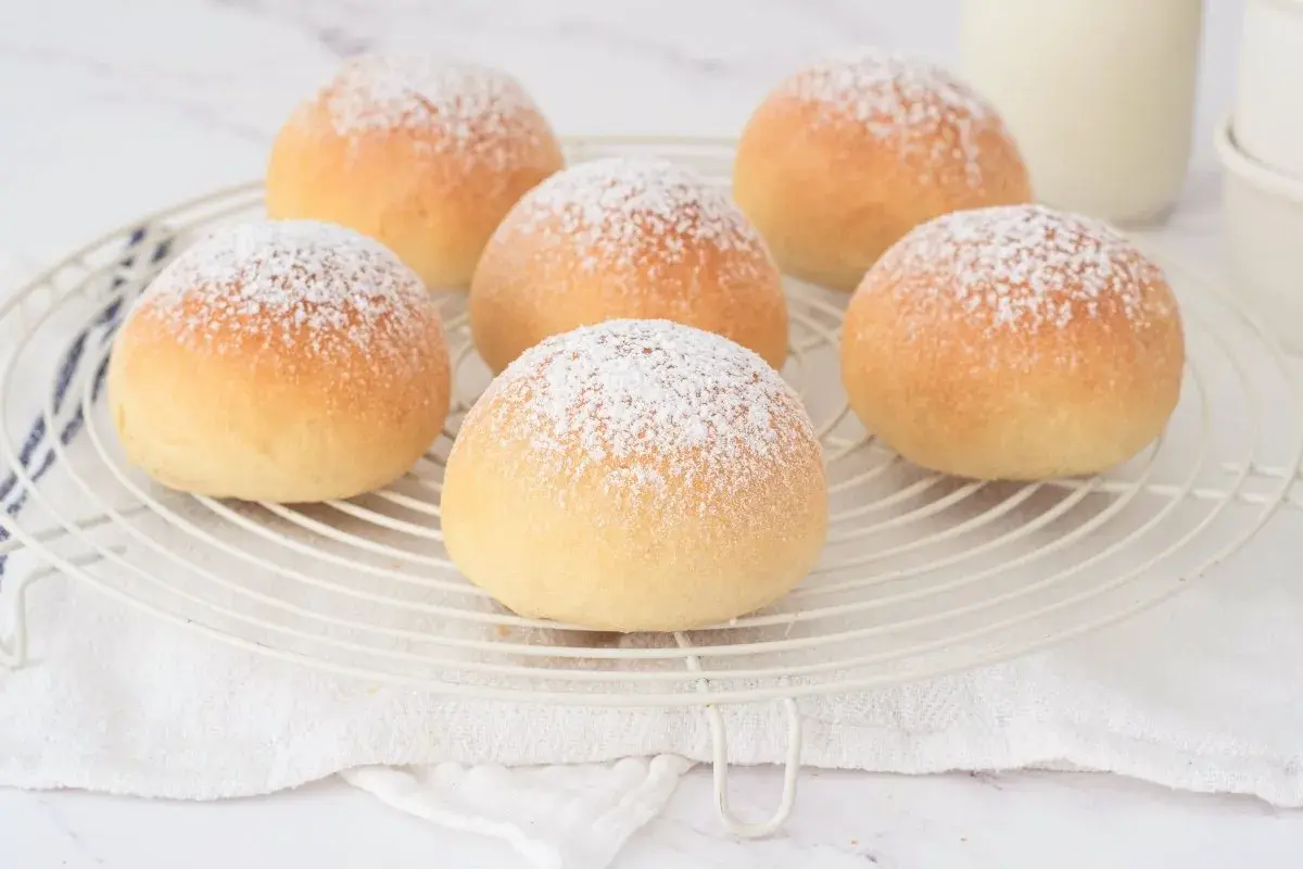 Seis deliciosas cocas de patata espolvoreadas con azúcar glas sobre una rejilla.
