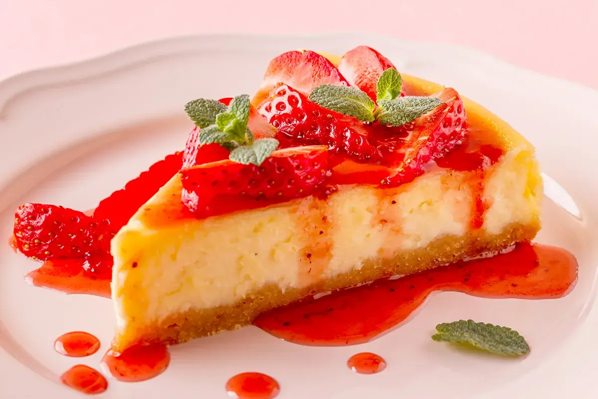 Deliciosa tarta de queso con fresas frescas y salsa de fresa, decorada con hojas de menta.