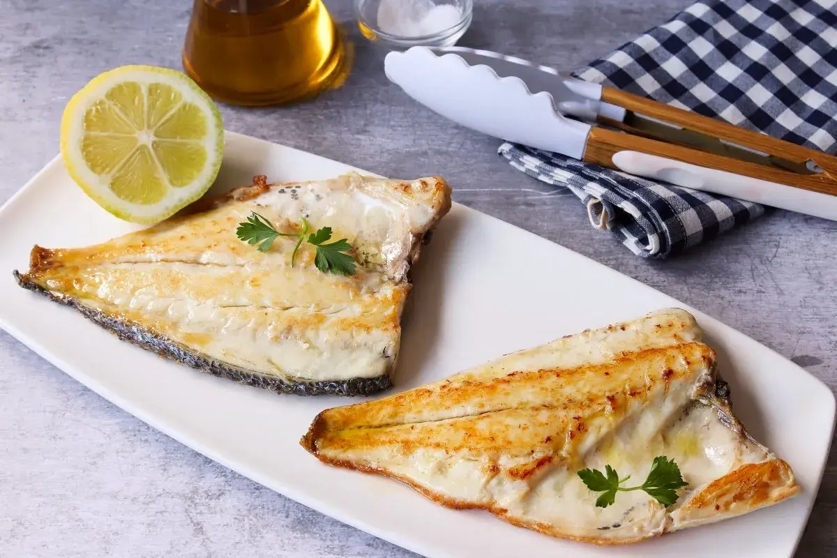 Dos filetes de dorada a la plancha, jugosos y dorados, servidos con perejil fresco y una rodaja de limón.