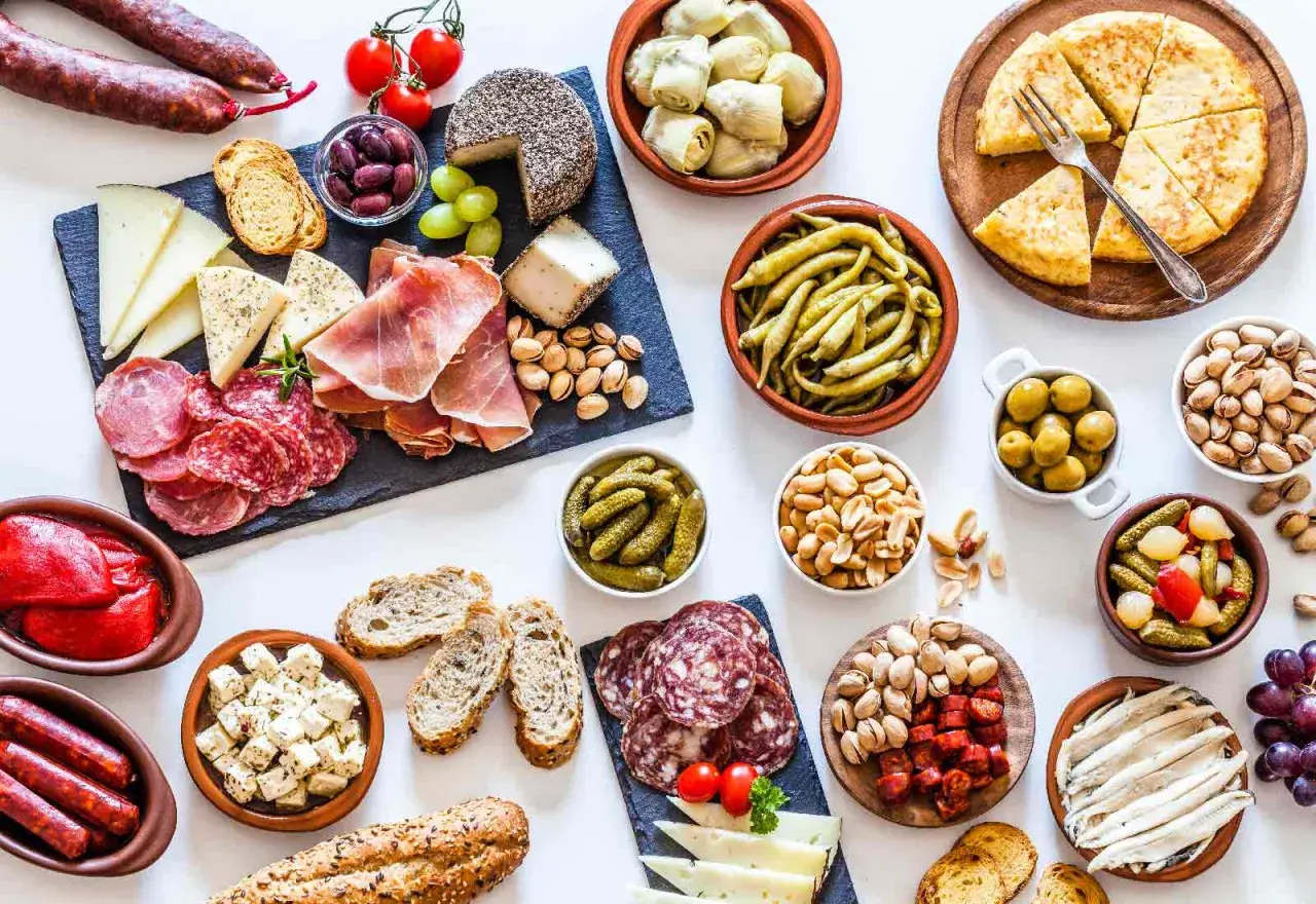 Gran variedad de aperitivos baratos para mucha gente: embutidos, quesos, aceitunas, frutos secos, pimientos, boquerones y tortilla.