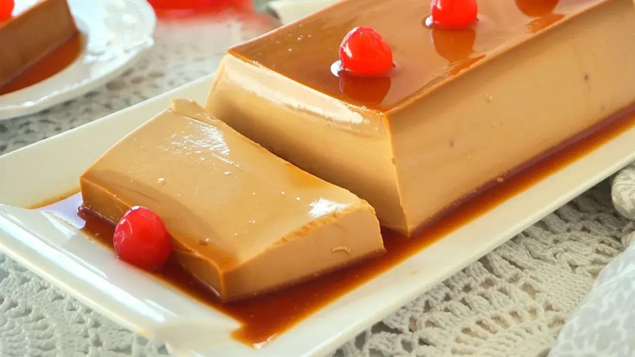 Un delicioso flan de café, con caramelo líquido y decorado con cerezas rojas, servido en un plato blanco.