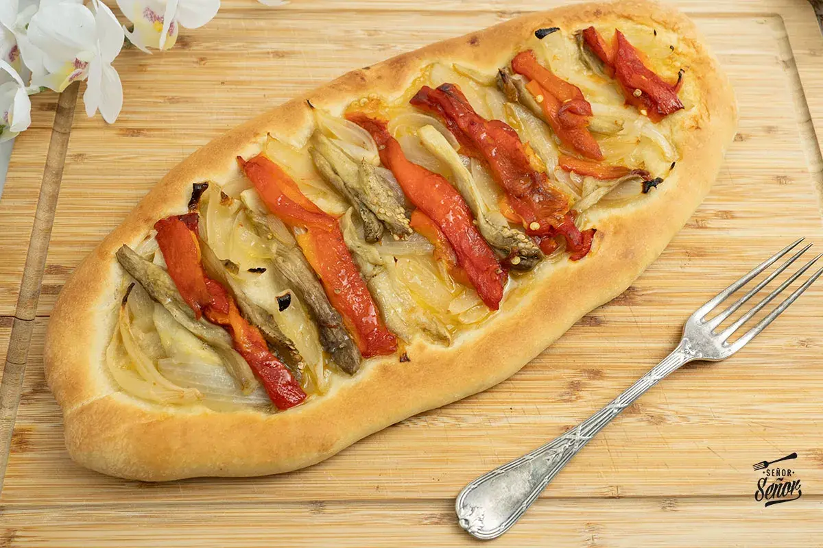 Coca de recapte con verduras asadas, pimientos rojos y cebolla sobre una base de pan rústico.