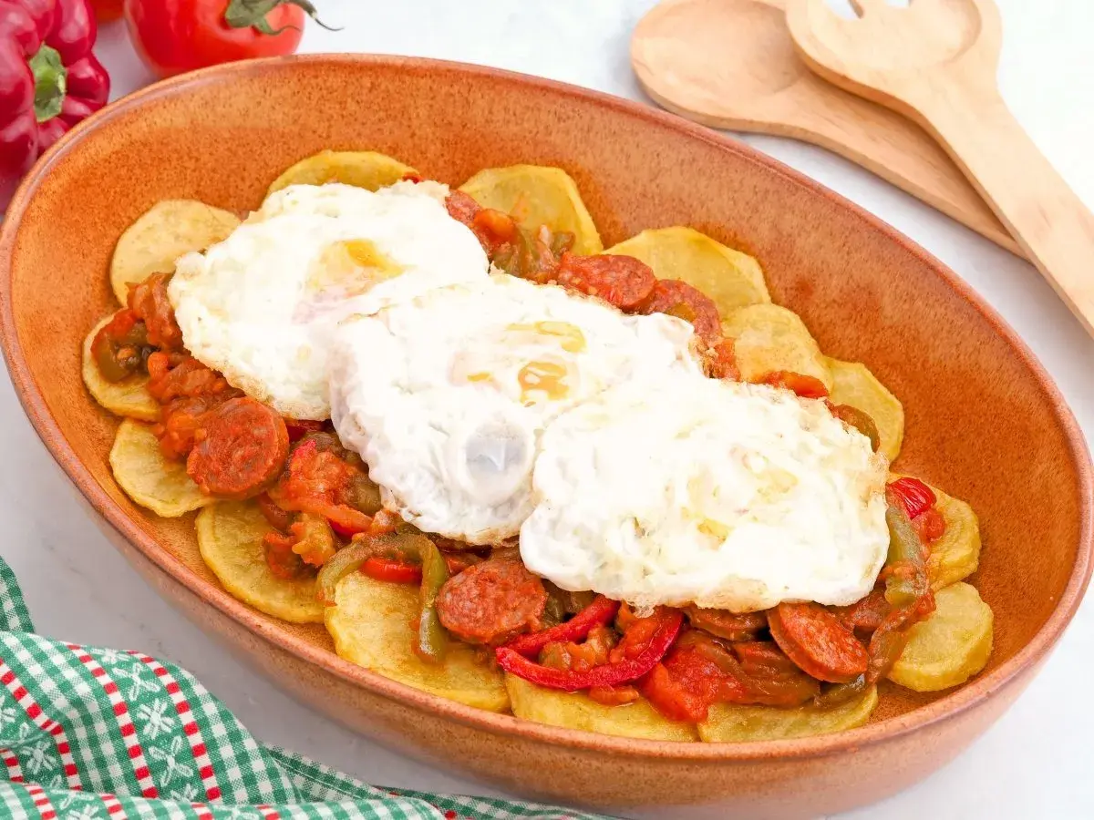 Huevos a la riojana servidos en una cazuela de barro, con patatas, chorizo y pimientos.