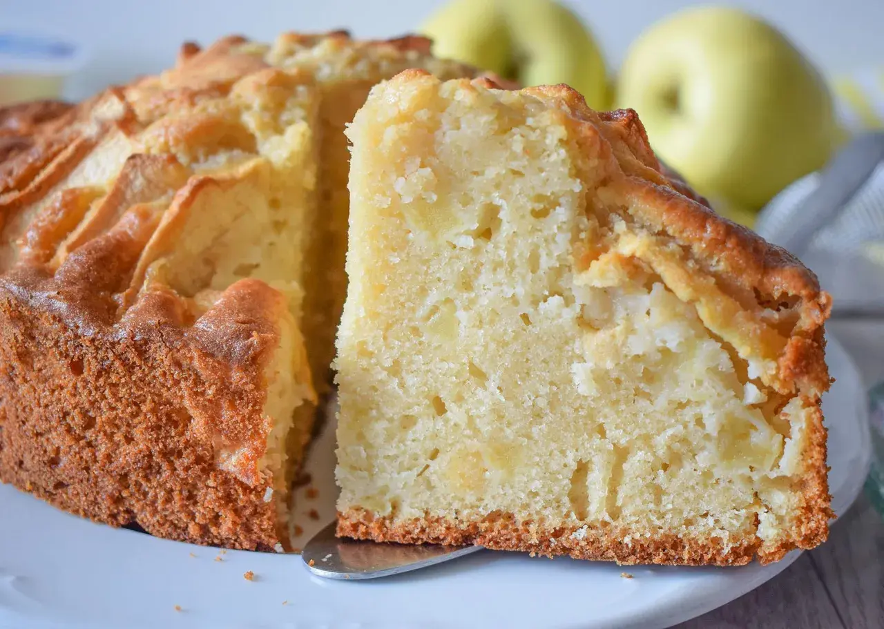 Un trozo de bizcocho de manzana casero, con trozos de fruta visibles en su interior tierno y dorado.