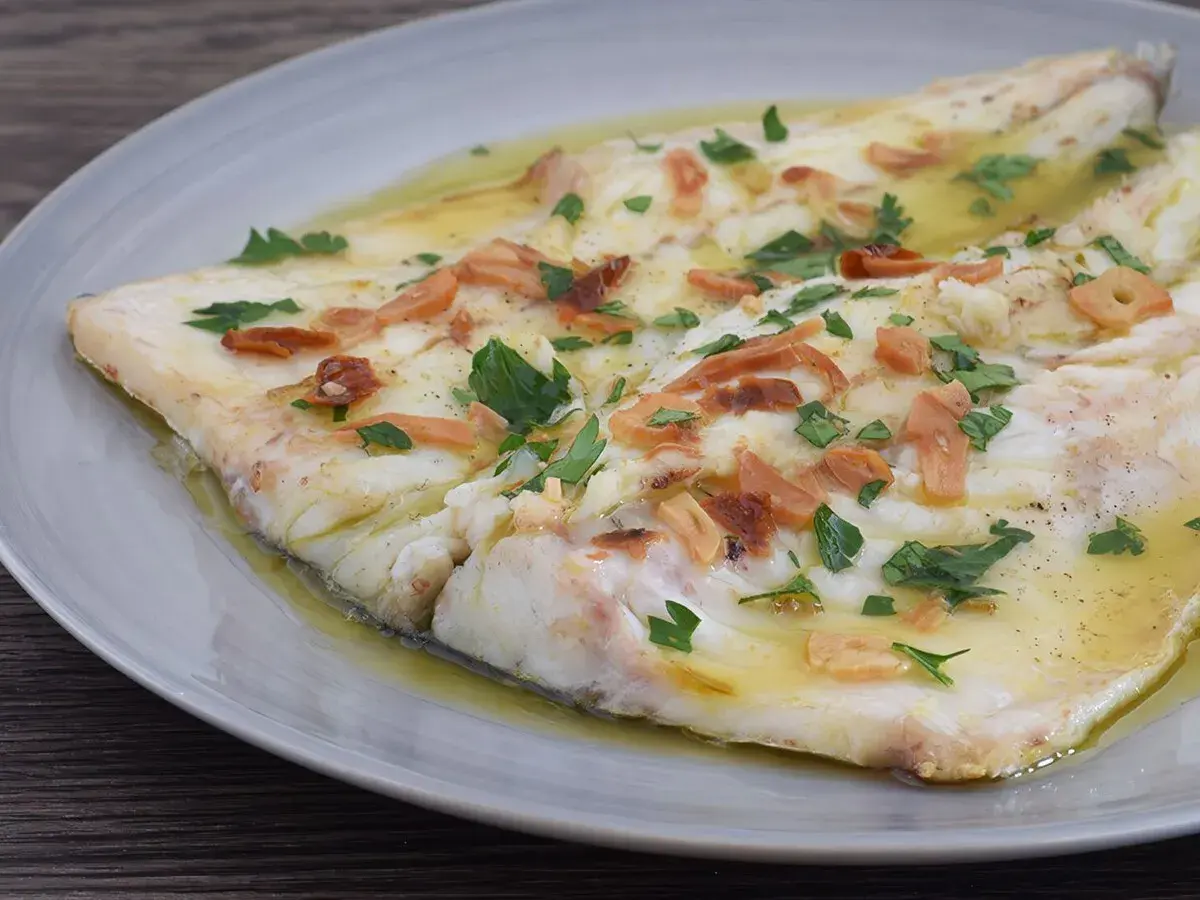 Lubina a la donostiarra, un plato de pescado blanco tierno bañado en aceite de oliva con láminas de ajo dorado y perejil fresco.