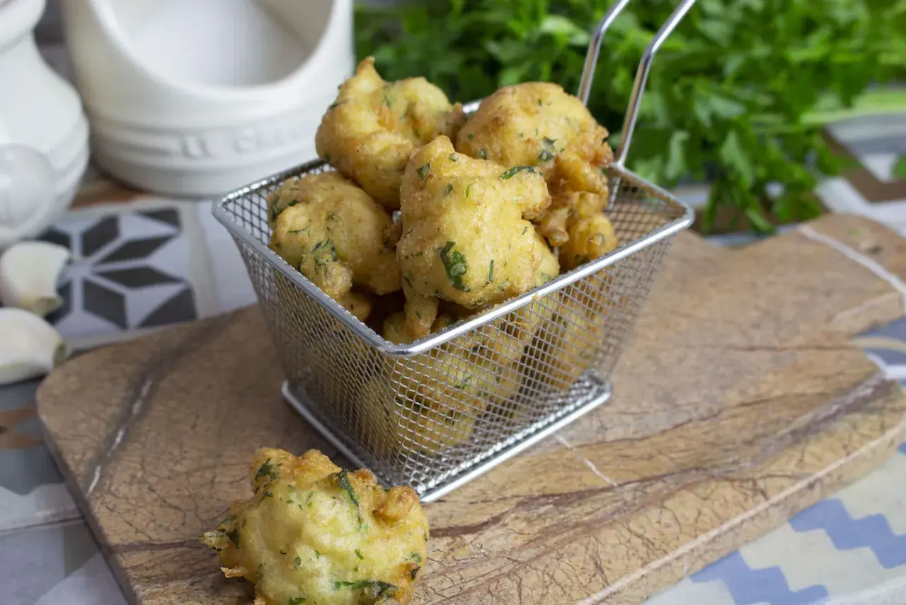 Buñuelos de bacalao dorados y crujientes, servidos en una cesta metálica. Perfectos para picar.