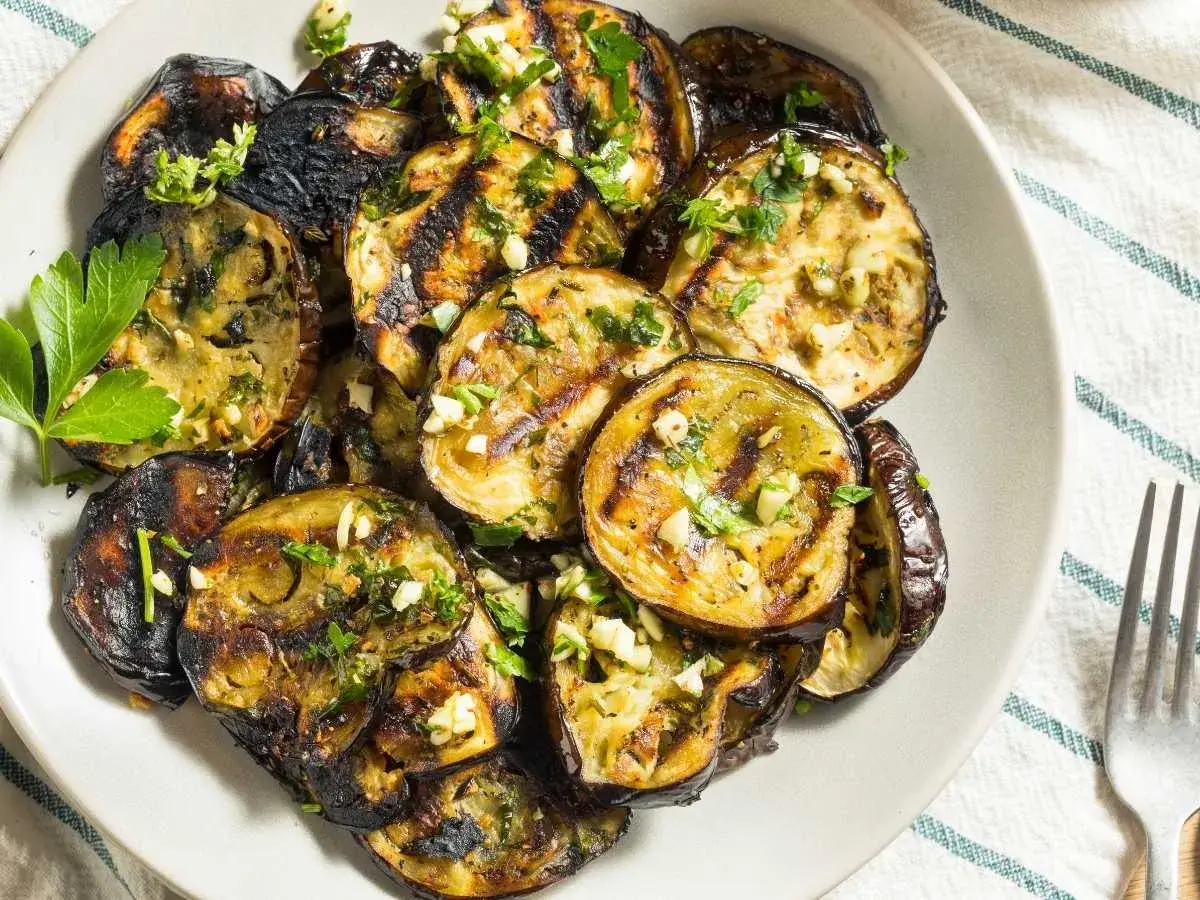 Rodajas de berenjena a la plancha, doradas y tiernas, con ajo picado y perejil fresco. Un plato delicioso y saludable.