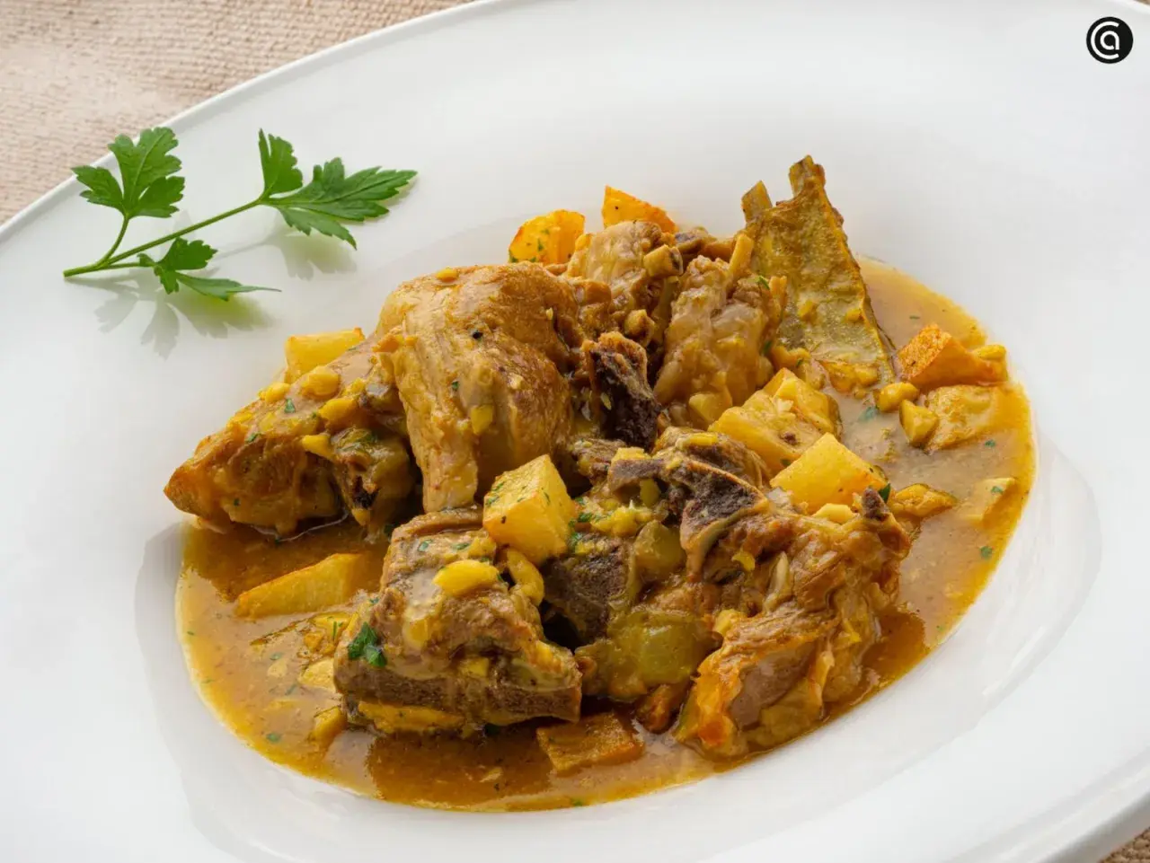 Choto al ajillo, un guiso tierno de cabrito con patatas y un toque de ajo, servido en un plato blanco.
