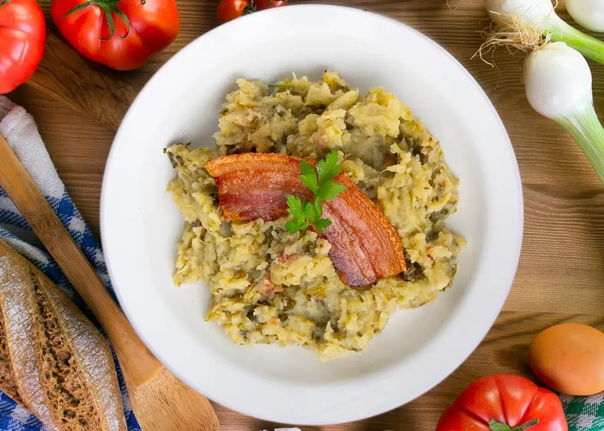 Un plato de trinxat de montaña con crujiente panceta y perejil. Acompañado de pan rústico, tomates y cebolletas.