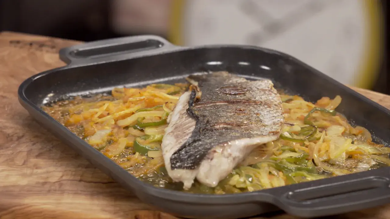 Filete de corvina a la roteña, con verduras salteadas en una sartén de hierro fundido.