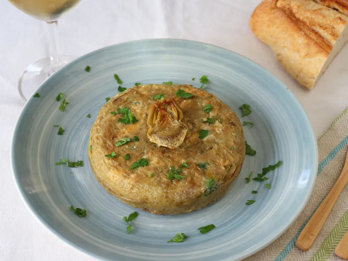 Tortilla de patatas con alcachofas de bote, decorada con perejil. Ideal para tus recetas con alcachofas de bote.