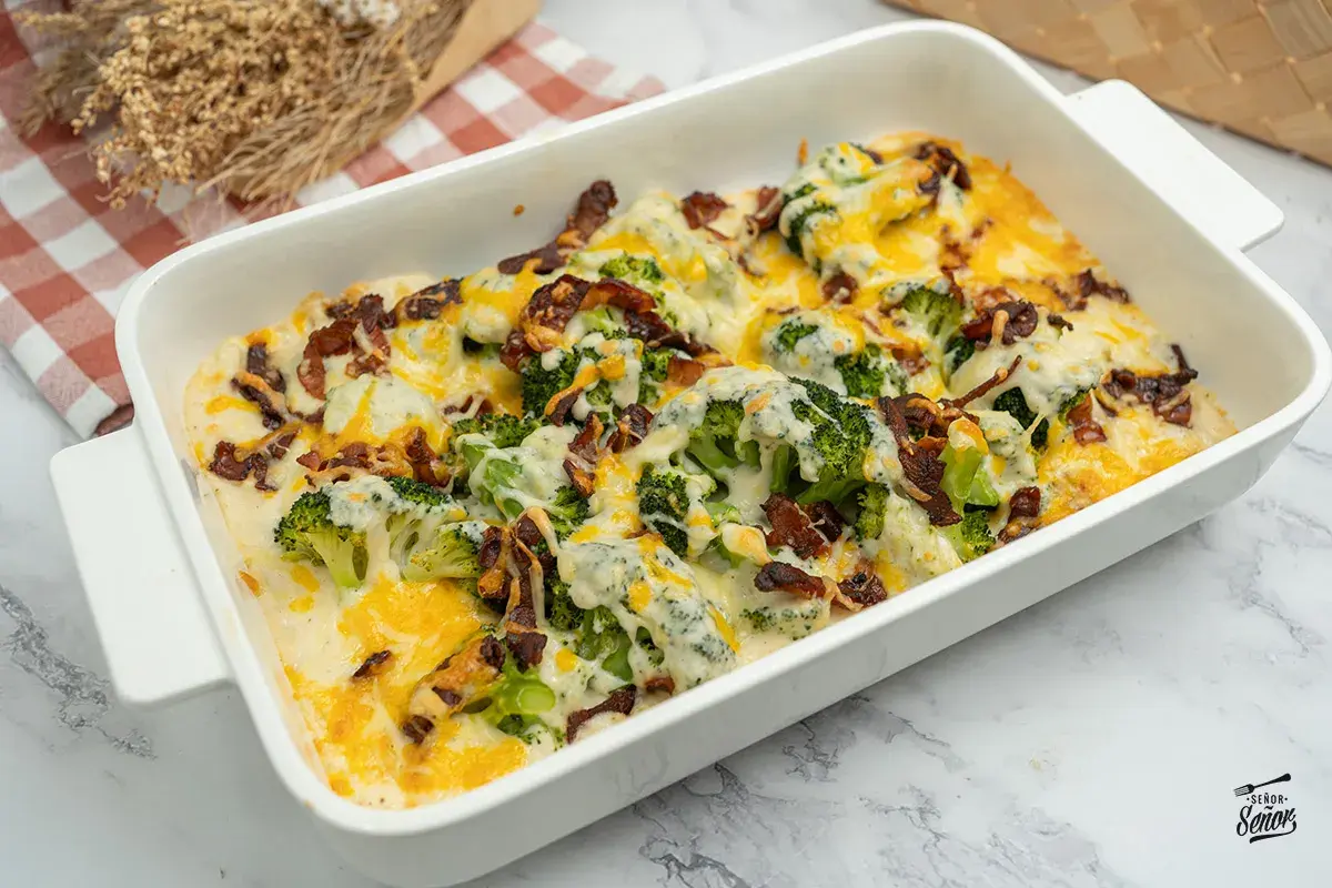 Delicioso brocoli al horno gratinado con queso y tocino crujiente, servido en una fuente blanca.