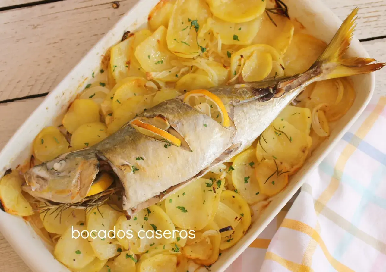 Un delicioso chicharro al horno con patatas, limón y romero, listo para servir.