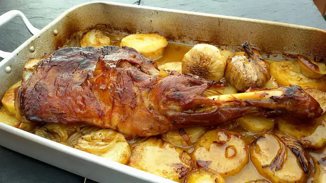 Paletilla de cordero lechal al horno estilo segoviano, dorada y jugosa, acompañada de patatas y ajos asados en su jugo.