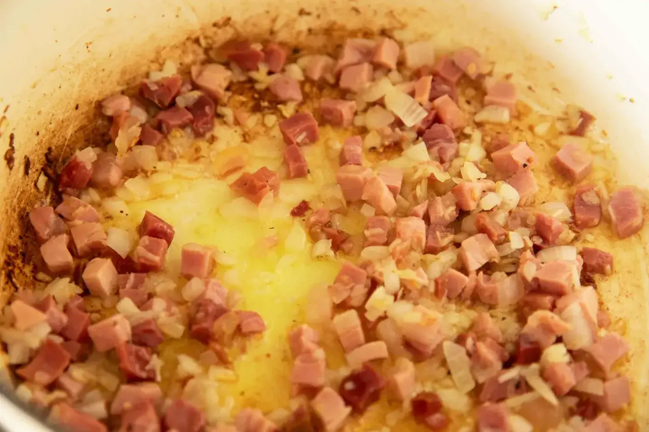 Guisantes con jamón, la receta de la abuela en plena cocción. Cebolla y taquitos de jamón dorándose en la sartén.