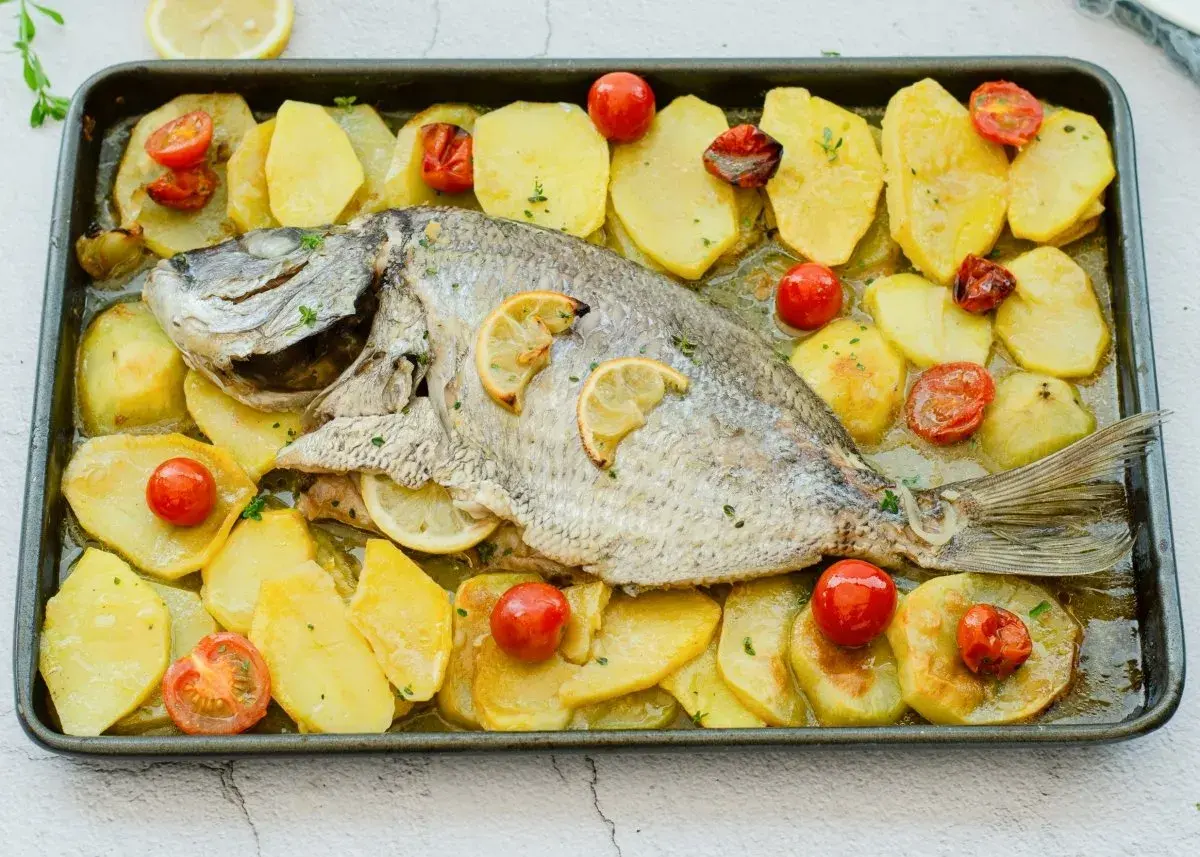 Delicioso sargo al horno con patatas y tomates cherry, listo para servir.