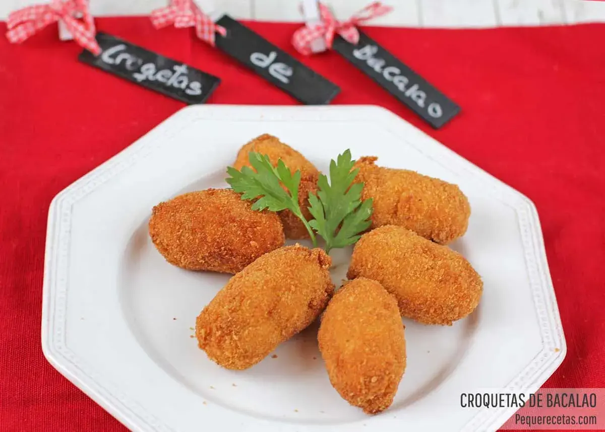 Croquetas de bacalao doradas y crujientes, servidas en un plato blanco con perejil.