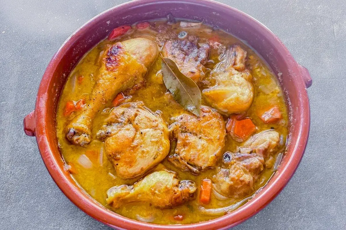 Delicioso pollo de corral guisado en cazuela de barro con zanahorias y laurel.