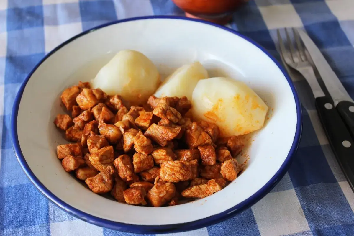 Plato de zorza con patatas cocidas, servido en un cuenco blanco con borde azul sobre un mantel de cuadros.